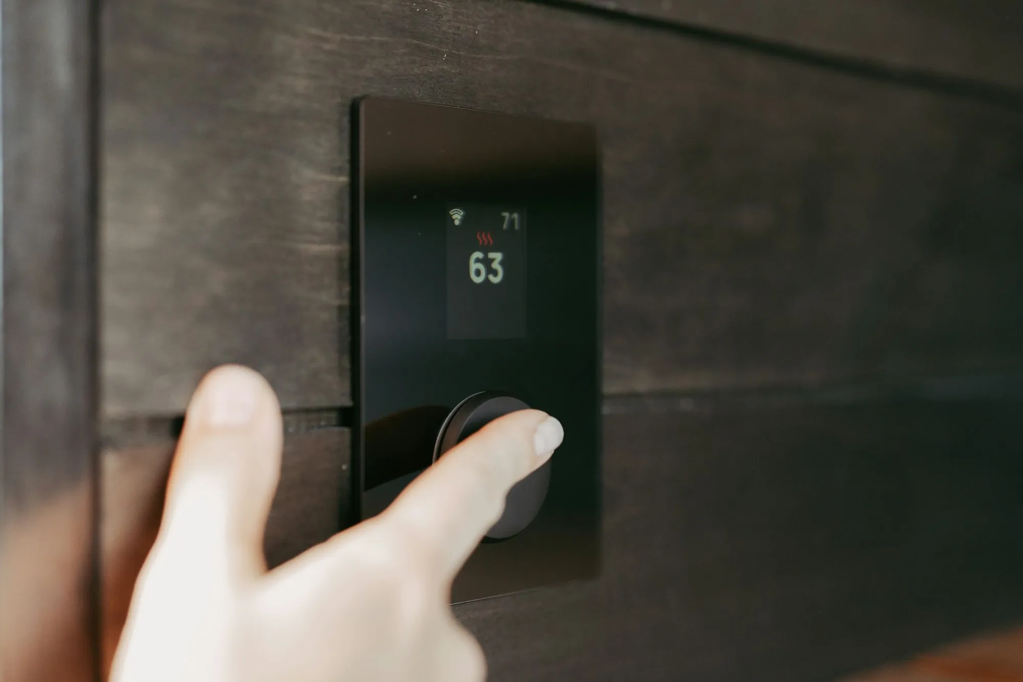 Finger turning a digital thermostat on a dark wall
